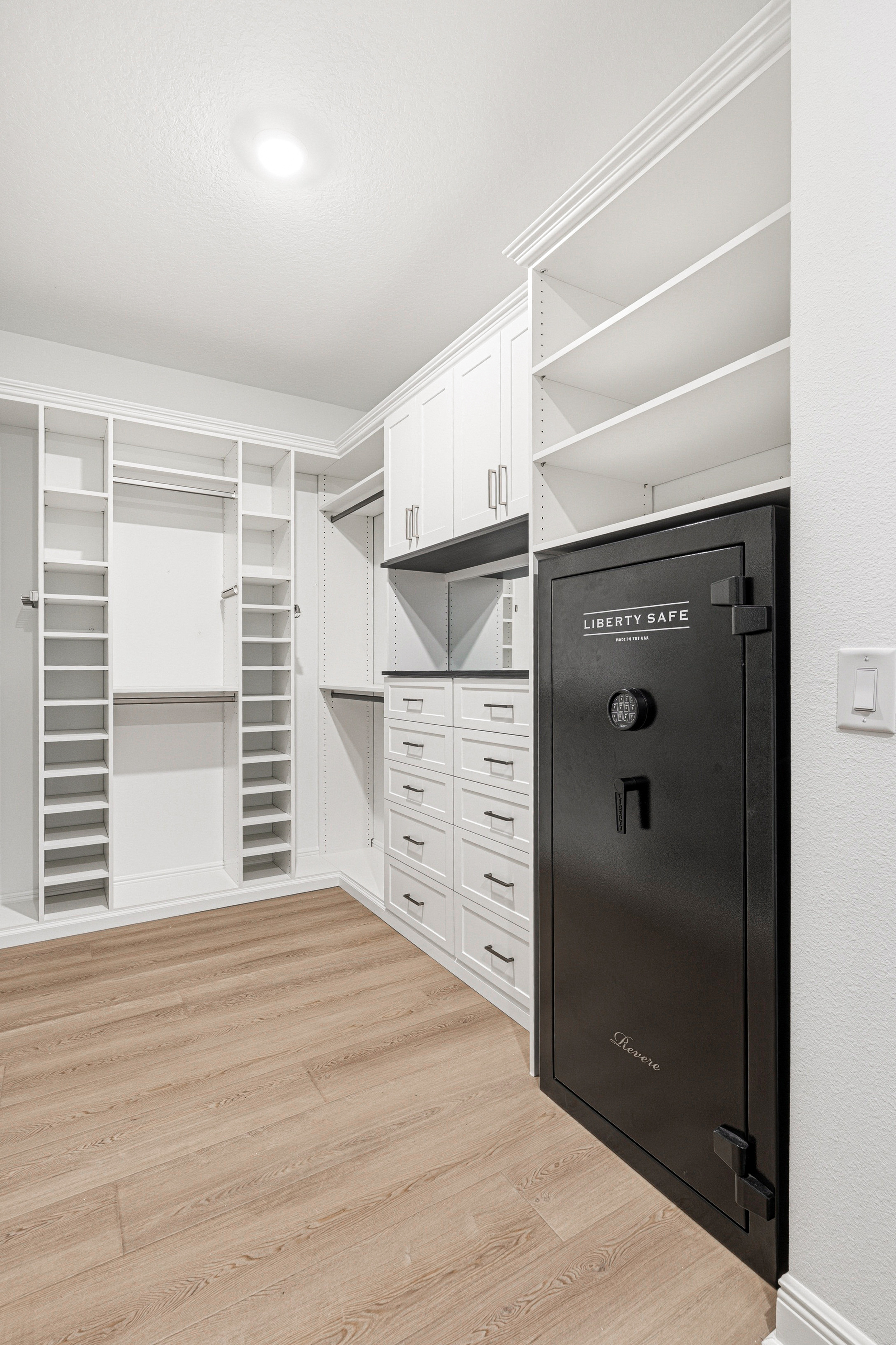 Walk-in closet with Liberty Safe built into custom white cabinetry and adjustable shelving in Bradenton FL